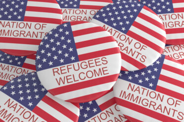 Pile of buttons with American flags that say Refugees Welcome and Nation of Immigrants