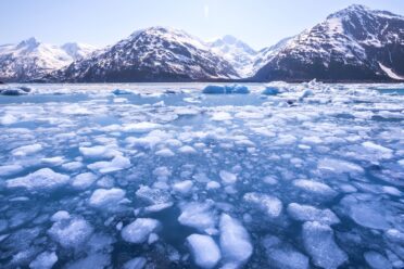 Snow capped mountains in the distance with a frozen lake melting