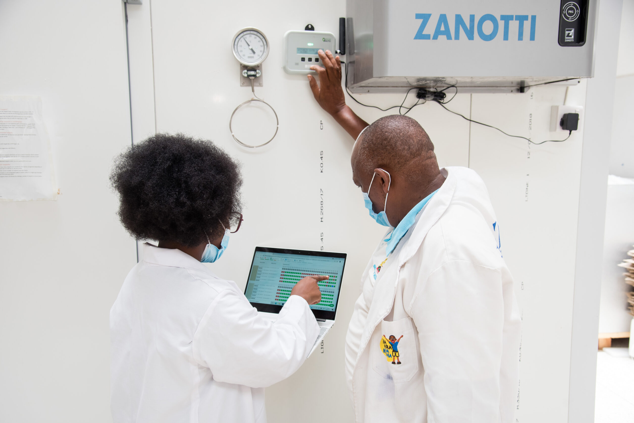 Two health care professionals wearing surgical masks looking at data on a laptop in a clinical setting